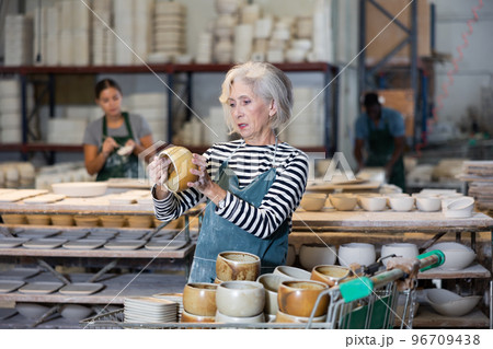 Mature woman ceramist arranging new bowls in workshop 96709438