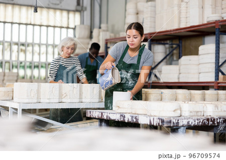 Pouring slip mass into plaster molds at pottery factory 96709574