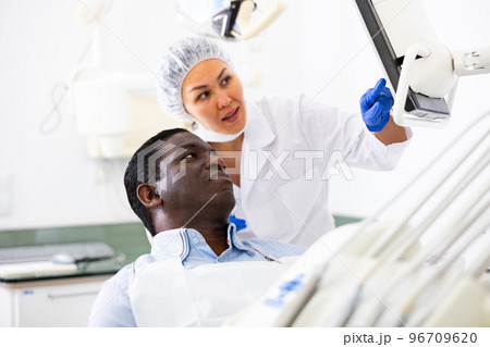 Man sitting on dental chair, female dentist pointing at display Man sitting on dental chair, female dentist pointing at display 96709620