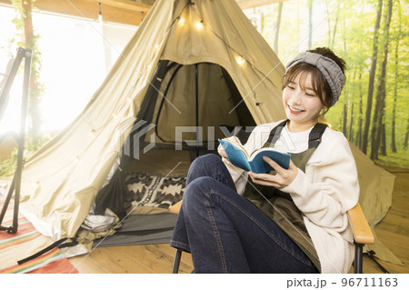 おうちキャンプイメージ　テントの前で読書をする若い女性　グランピングカフェ 96711163