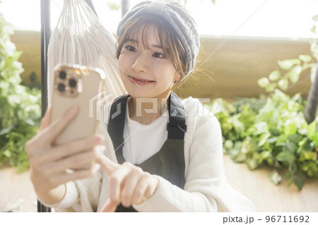 ハンモックに座ってスマホを見る若い女性　　家キャン おうちキャンプ　キャンプイメージ 96711692