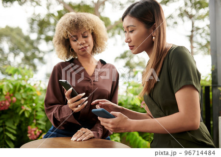 Woman showing application of new online shop to friend Woman showing application of new online shop to friend 96714484