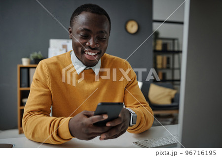 African American businessman typing message on smartphone and smiling while sitting at his workplace at office 96716195