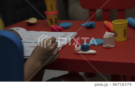 A 6 years old boy sits at a table and sculpts a snail from colored plasticine A 6 years old boy sits at a table and sculpts a snail from colored plasticine 96716374