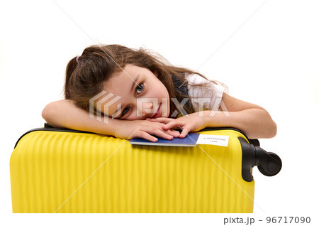 Isolated portrait on white background of lovely baby girl, little traveler with boarding pass and suitcase, looking dreamily at camera, traveling abroad for the weekend. Tourism and air travel concept 96717090