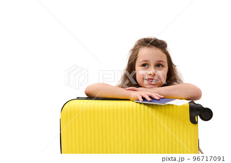 Adorable little passenger girl, with boarding pass and suitcase, traveling abroad for the weekend, smiling toothy smile, dreamily looking away at advertising space. Tourism Tourney Air travel concept Adorable little passenger girl, with boarding pass and suitcase, traveling abroad for the weekend, smiling toothy smile, dreamily looking away at advertising space. Tourism Tourney Air travel concept 96717091