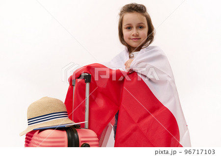 Caucasian cute child, lovely baby girl with pink suitcase, wrapping in Polish or Canadian flag, going on summer holidays, isolated over white background, ad space. Flight Travel Trip Tourism concept 96717103