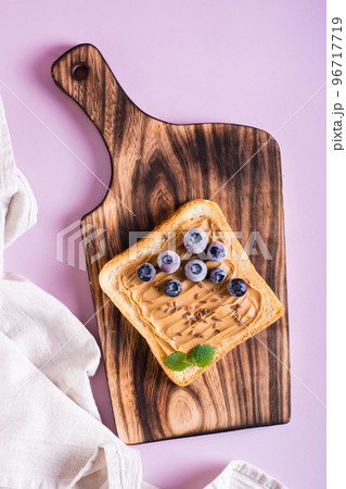 Peanut butter toast with blueberries, flax seeds and mint on a cutting board. Top and vertical view. 96717719