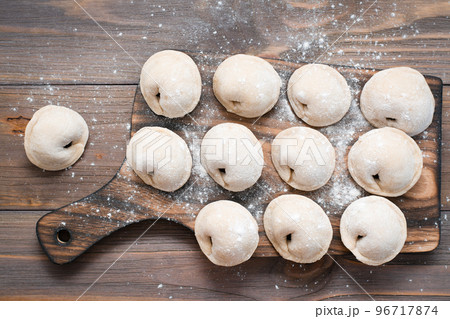 Raw dumplings ready for cooking lie in rows on a wooden cutting board on the table. Top view Raw dumplings ready for cooking lie in rows on a wooden cutting board on the table. Top view 96717874