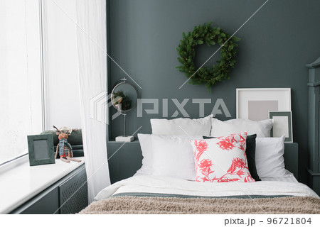 Stylish Christmas bedroom. Pillows on the bed and a wreath on the wall Stylish Christmas bedroom. Pillows on the bed and a wreath on the wall 96721804
