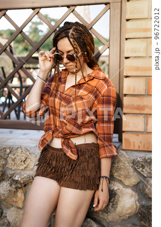 a girl with a dreadlocked hairstyle poses in summer outdoor, bright sunlight, dressed in a plaid shirt and shorts a girl with a dreadlocked hairstyle poses in summer outdoor, bright sunlight, dressed in a plaid shirt and shorts 96722012