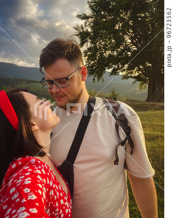 a couple stands under a big old beech tree with a view of the mountains and the sunset 96723562