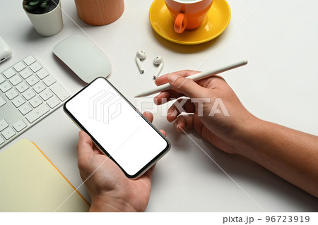 Above view of man hands holding smart phone over his working desk. Copy space, blank screen for your advertise 96723919