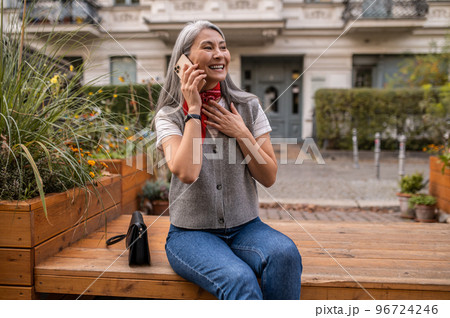 Long-haired woman sitting on the bench and talking on the phone Long-haired woman sitting on the bench and talking on the phone 96724246