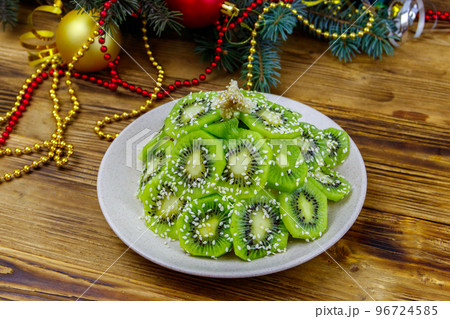 Christmas tree shaped fruit salad and Christmas decorations on wooden table. Creative idea for Christmas and New Year festive desserts. Funny food idea for kids 96724585