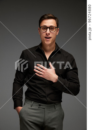 Surprised young man in black business classic style shirt and grey trousers looking at camera with surprise isolated over grey background. Modern office style 96724880