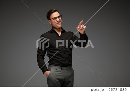 Smiling young man in black business classic style shirt and grey trousers posing isolated over grey background. Fashion look of businessman. Office style Smiling young man in black business classic style shirt and grey trousers posing isolated over grey background. Fashion look of businessman. Office style 96724886