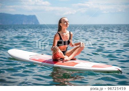 Woman sap sea. Sports girl on a surfboard in the sea on a sunny summer day. In a black bathing suit, he sits on a sapa in the sea. Rest on the sea. 96725459
