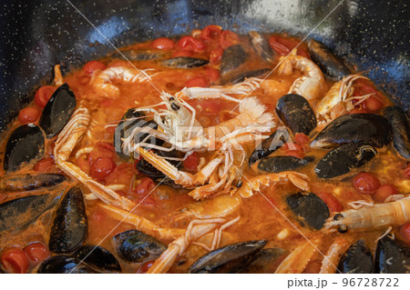 Cooking Italian stew with seafood and tomatoes in a big frying pan, close up Cooking Italian stew with seafood and tomatoes in a big frying pan, close up 96728722