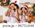 Happy ethnic children on Christmas eve,   girl and boy covers eyes with cookies gingerbreads that they baked and laughs  in cozy kitchen 96731046