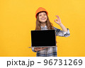 happy teen girl in helmet and checkered shirt presenting laptop, ok 96731269