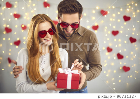 Loving couple unpacks a gift for Valentine's Day standing on a background of garlands and hearts. 96731327