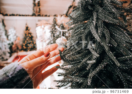 Woman chooses artificial Christmas tree for New Year 2023 celebration. Christmas decor to decorate interior decor for winter holidays. Shopping, buying gifts. Female hand touching a toy Christmas tree Woman chooses artificial Christmas tree for New Year 2023 celebration. Christmas decor to decorate interior decor for winter holidays. Shopping, buying gifts. Female hand touching a toy Christmas tree 96731469
