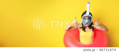 Funny happy woman in swimming ring, wearing snorkling mask for diving, showing thumbs up, good approval gesture, posing against yellow background Funny happy woman in swimming ring, wearing snorkling mask for diving, showing thumbs up, good approval gesture, posing against yellow background 96731674