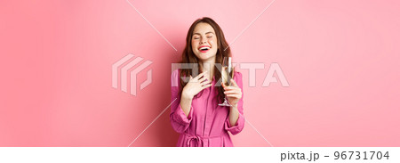 Celebration and holidays concept. Stylish coquettish woman in trendy dress, holding glass of champagne at party, smiling pleased, standing over pink background 96731704