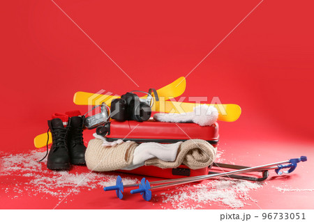 Suitcase with warm clothes, camera and skis on red background. Winter vacation 96733051