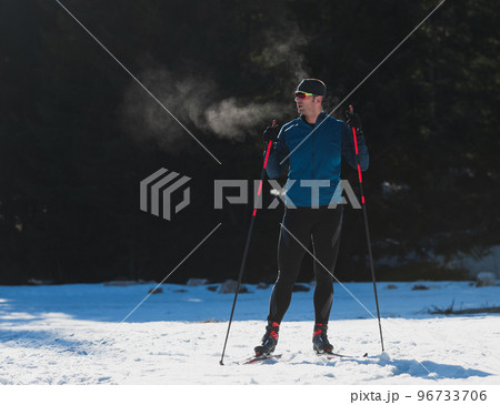 Portrait handsome male athlete with cross country skis, taking fresh breath and having break after hard workout training in a snowy forest. Healthy winter lifestyle concept Portrait handsome male athlete with cross country skis, taking fresh breath and having break after hard workout training in a snowy forest. Healthy winter lifestyle concept 96733706