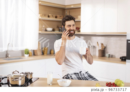 Happy adult caucasian guy with beard in white t-shirt drinks cup of coffee, calls by phone 96733717