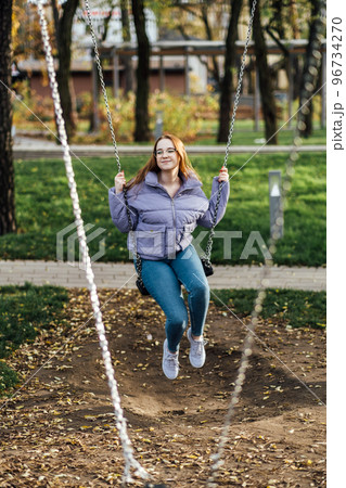 Candid Portrait of beautiful young woman on swing on spring day outdoors. Happy student teenager girl in glasses on swing in city park. Candid Portrait of beautiful young woman on swing on spring day outdoors. Happy student teenager girl in glasses on swing in city park. 96734270
