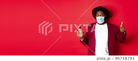 Covid-19, quarantine and holidays concept. Young african american man in medical mask, showing hand sanitizer and thumb up, recommending to use antiseptic 96738793