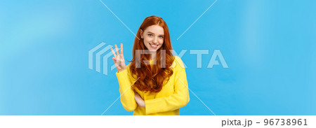 Gorgeous young redhead girl 20s in yellow sweater, smiling carefree making order, reservetion for three people, showing number third with fingers, standing blue background Gorgeous young redhead girl 20s in yellow sweater, smiling carefree making order, reservetion for three people, showing number third with fingers, standing blue background 96738961
