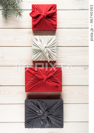 Group of christmas presents in furoshiki package, top view. Spruce branch and gift boxes on white planking. Objects layout in ascending size. Christmas or New Year holiday, eco decor, zero waste Group of christmas presents in furoshiki package, top view. Spruce branch and gift boxes on white planking. Objects layout in ascending size. Christmas or New Year holiday, eco decor, zero waste 96740365