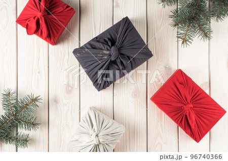 Composition of christmas presents in furoshiki package, top view. Spruce branches and gift boxes on white planking. Objects layout. Christmas or New Year holiday, eco decor, zero waste Composition of christmas presents in furoshiki package, top view. Spruce branches and gift boxes on white planking. Objects layout. Christmas or New Year holiday, eco decor, zero waste 96740366