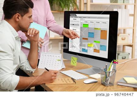Colleagues working with calendar app on computer in office Colleagues working with calendar app on computer in office 96740447