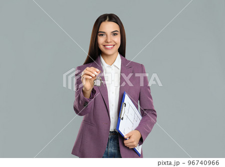 Female real estate agent with key and clipboard on grey background Female real estate agent with key and clipboard on grey background 96740966