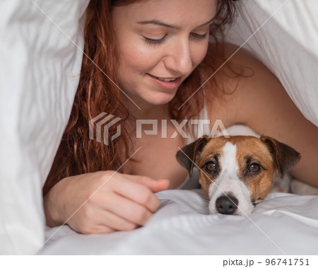 Caucasian red-haired woman sleeps in an embrace with a jack russell terrier dog on a white sheet. Caucasian red-haired woman sleeps in an embrace with a jack russell terrier dog on a white sheet. 96741751