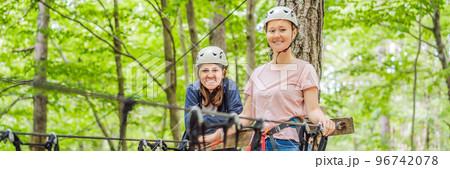 BANNER, LONG FORMAT Two women girls female gliding climbing in extreme road trolley zipline in forest on carabiner safety link on tree to tree top rope adventure park. Family weekend children kids 96742078