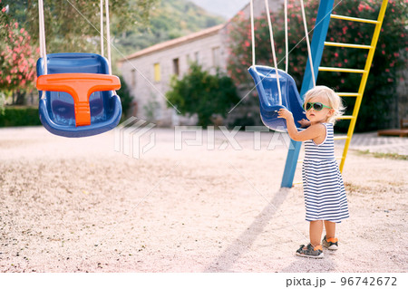 Little girl in sunglasses stands near the swing on the playground. High quality photo Little girl in sunglasses stands near the swing on the playground. High quality photo 96742672