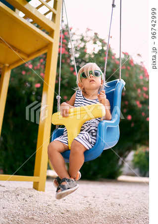 Little girl sits on a swing on the playground against the backdrop of a rose bush. High quality photo 96742999