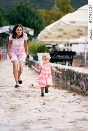 Smiling mother follows little girl on paving stones. High quality photo Smiling mother follows little girl on paving stones. High quality photo 96743184