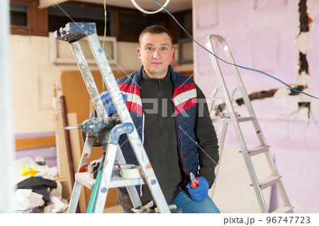 Portrait of an electrician with pliers in his hands in house under construction Portrait of an electrician with pliers in his hands in house under construction 96747723