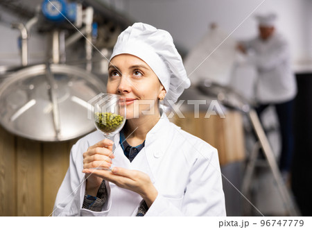 Portrait of a positive female brewer with a glass of hops at brewery Portrait of a positive female brewer with a glass of hops at brewery 96747779
