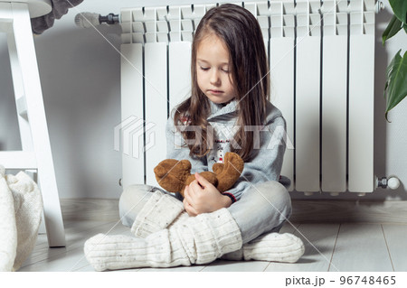 Calm independent nice little girl warming up near heating radiator and play with stuffed soft bear toys and having fun Calm independent nice little girl warming up near heating radiator and play with stuffed soft bear toys and having fun 96748465