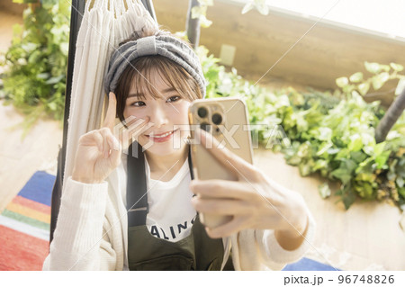 ハンモックに寝てスマホで自撮りをする若い女性　　家キャン おうちキャンプ　キャンプイメージ 96748826