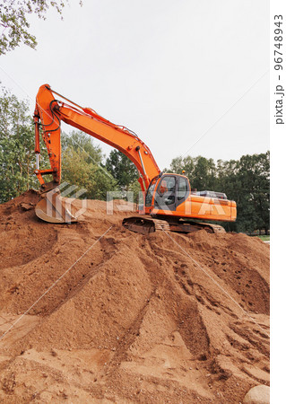 orange tractor or excavator with a bucket on the sand. a large working machine for laying sewers and communal communications orange tractor or excavator with a bucket on the sand. a large working machine for laying sewers and communal communications 96748943