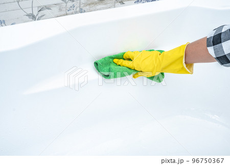 cleaning white acrylic bathtub in bathroom. Hand in yellow glove wipes tub with green microfiber cloth. copy space cleaning white acrylic bathtub in bathroom. Hand in yellow glove wipes tub with green microfiber cloth. copy space 96750367